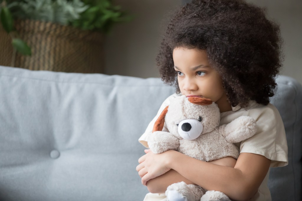 Lonely, sad African American girl hugging a teddy bear, looking away, illustrating childhood loneliness and the need for charity and adoption