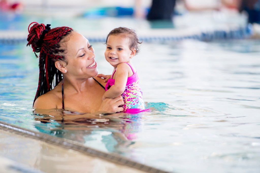 Mother teaches her daughter to swim in an indoor pool at a health club